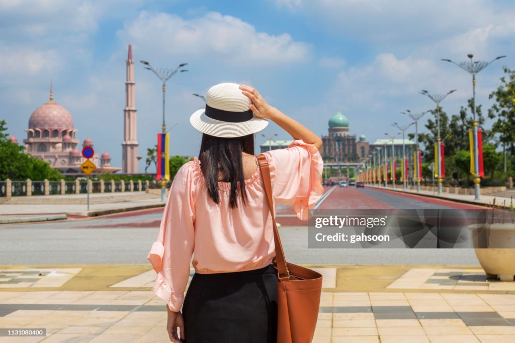Rear view of Young Asian traveling women walking and looking around the Putrajaya area, with the background of Islamic Mosque and the administrition Office of the Prime Minister of Malaysia