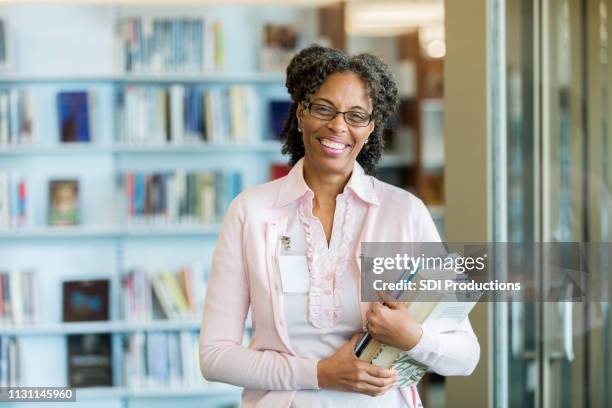 portrait of cheerful female librarian holding books - portrait of teacher and student stock pictures, royalty-free photos & images