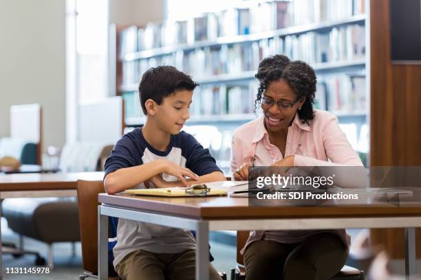 middle school age boy reads with mentor in library - coach imagens e fotografias de stock