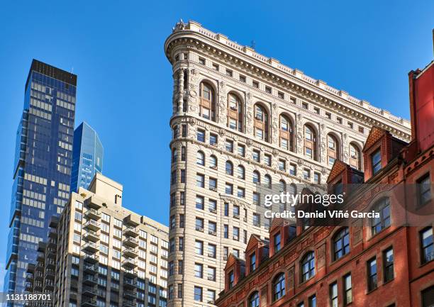 side view of the flatiron building with surrounding buildings in the background against a blue sky - flat iron stock pictures, royalty-free photos & images