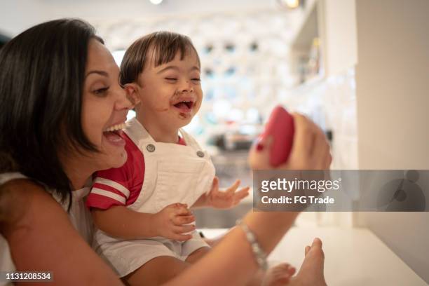 moeder en down syndroom zoon het nemen van een selfie na het eten van chocolade - down syndrome baby stockfoto's en -beelden