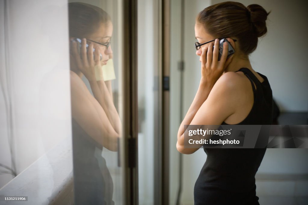 Woman standing by window, holding mobile phone to ear