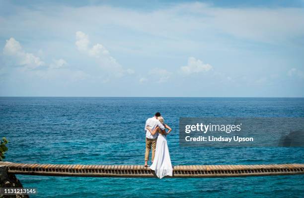 couple in wedding attire, embracing, standing on bridge over sea, looking out to sea, rear view - jamaika stock pictures, royalty-free photos & images