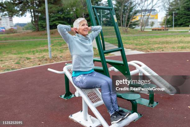 mature woman with grey hair exercising at outdoor gym - outdoor gym stock pictures, royalty-free photos & images