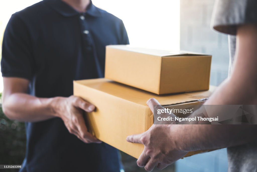 Midsection Of Delivery Person Giving Boxes To Young Man At Home