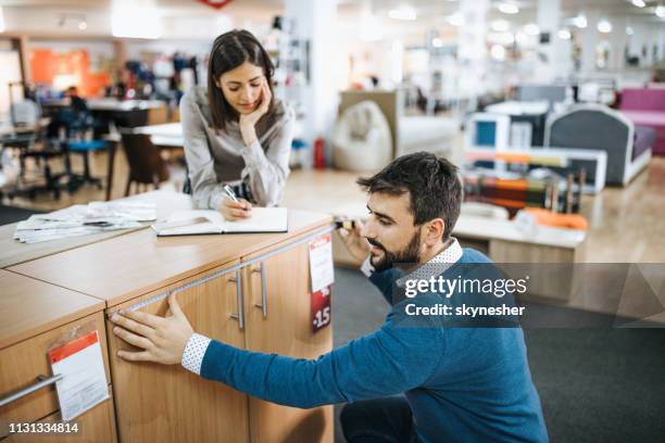 smiling workers taking measurements of a piece of furniture while working at the store. - furniture shopping stock pictures, royalty-free photos & images