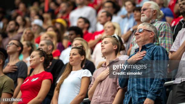 zuschauer singen nationalhymne im stadion - nationalhymne stock-fotos und bilder
