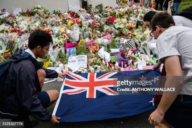 Students display the New Zealand national flag next to flowers during a vigil in Christchurch on March 18 three days after a shooting incident at two...