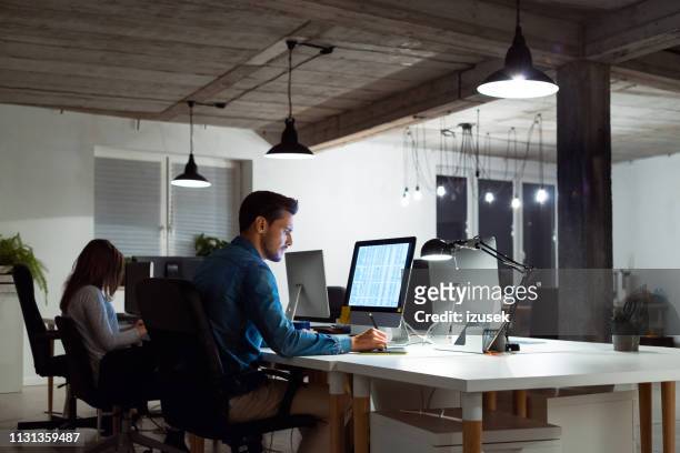 businessman using computer by female colleague - angle poise lamp stock pictures, royalty-free photos & images