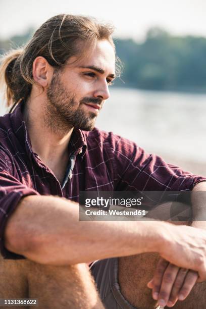 confident young man sitting at the riverside - long hair photos stock-fotos und bilder