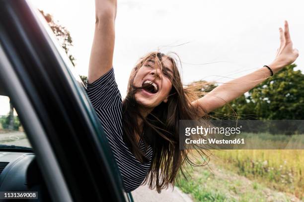 carefree young woman leaning out of car window screaming - driving fun stock pictures, royalty-free photos & images