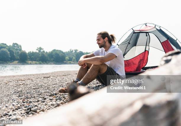 young man sitting at a tent at the riverside - water cooler stock-fotos und bilder