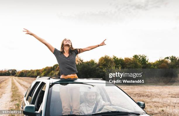 carefree young woman looking out of sunroof of a car - fun to drive stockfoto's en -beelden