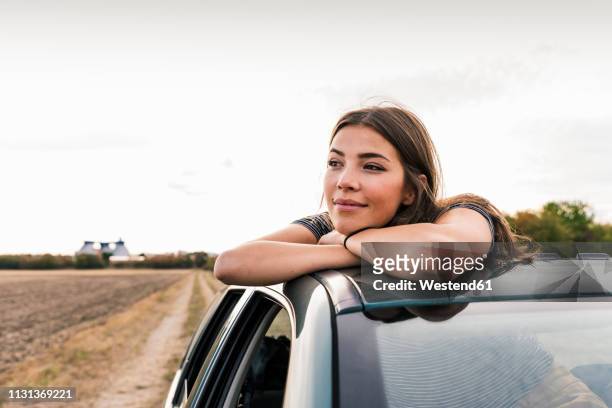 smiling young woman looking out of sunroof of a car - rijden een motorvoertuig besturen stockfoto's en -beelden