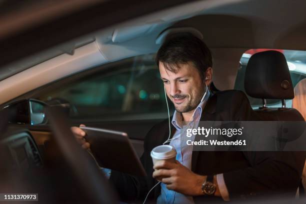 businessman sitting in car at night, using digital tablet, drinking coffee - car listening to music imagens e fotografias de stock