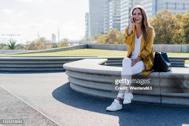 happy woman with bag and cell phone sitting on a bench in the city - 40 2018 stock pictures, royalty-free photos & images