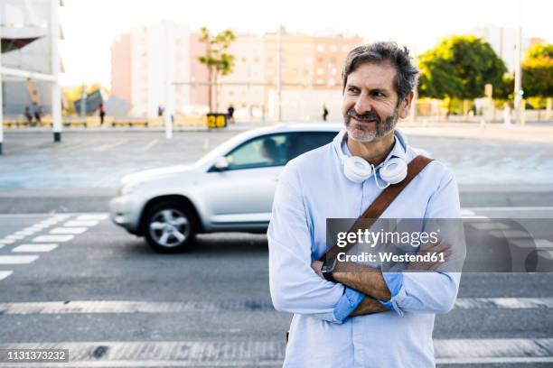 portrait of smiling mature man with headphones standing at a street - car reflection stock-fotos und bilder