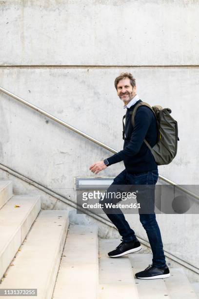 smiling mature man with a backpack walking up stairs in the city - 階段　のぼる ストックフォトと画像