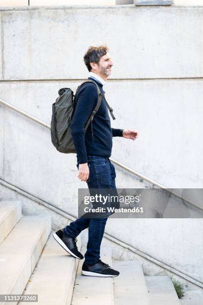 smiling mature man with a backpack walking down stairs in the city - walking side view stock pictures, royalty-free photos & images