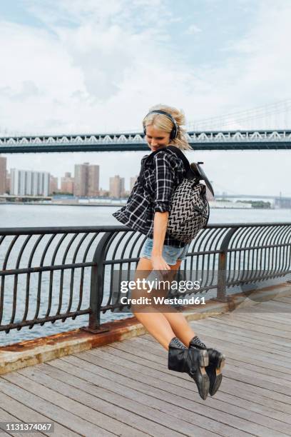 usa, new york city, brooklyn, happy young woman with headphones and cell phone jumping at the waterfront - shallow 2018 song stock pictures, royalty-free photos & images