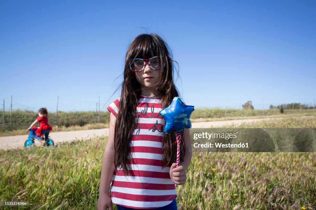 Two girls with bicycle and star-shaped wand in remote landscape