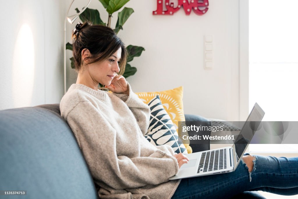 Woman sitting on her couch, surfing the net, using laptop