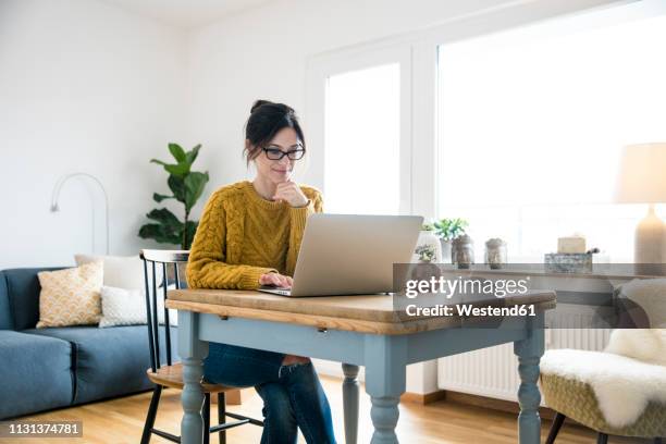 woman sitting at table, using laptop - woman laptop stock-fotos und bilder