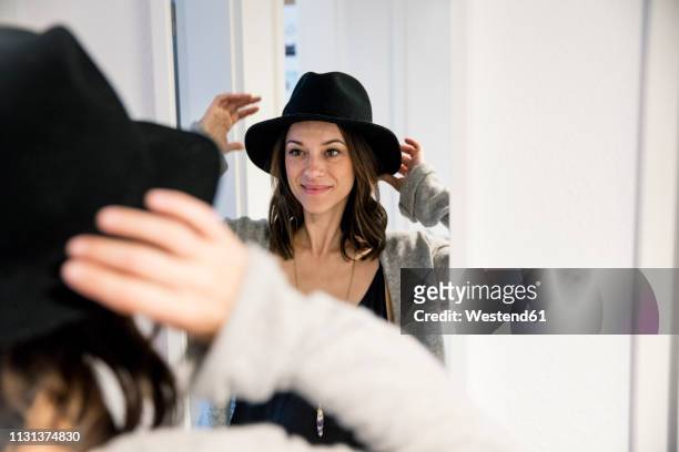 mature woman standing in front of mirror , putting on a hat - making stock-fotos und bilder