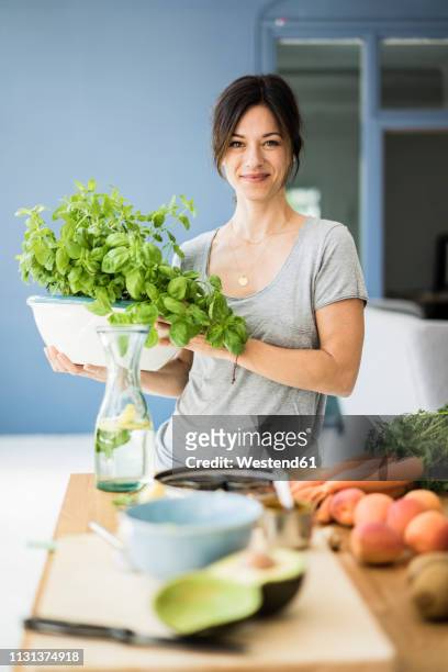 woman standing in kitchen, holding pot of basil - mature woman herbs stock pictures, royalty-free photos & images