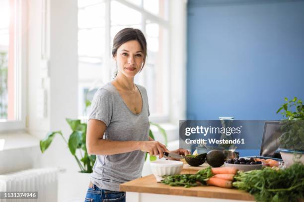 woman preparing healthy food in her kitchen - woman portrait kitchen laptop stock-fotos und bilder