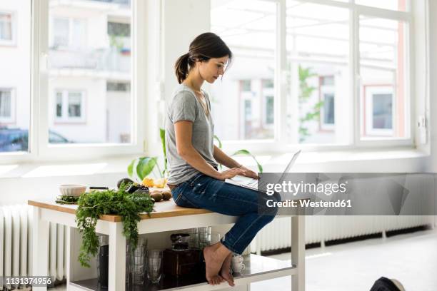 woman sitting on kitchen table, searching for healthy recipes, using laptop - suchen laptop stock-fotos und bilder