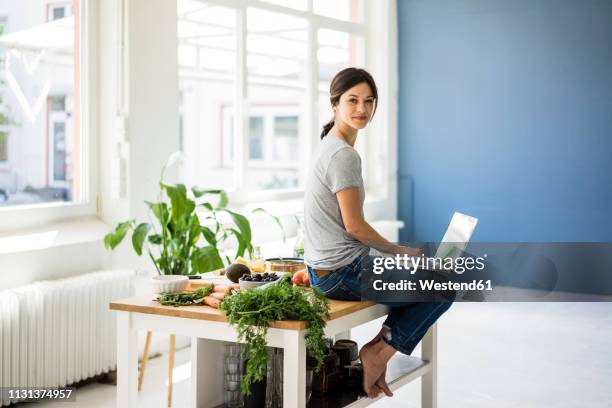 woman sitting on kitchen table, searching for healthy recipes, using laptop - woman portrait kitchen laptop bildbanksfoton och bilder