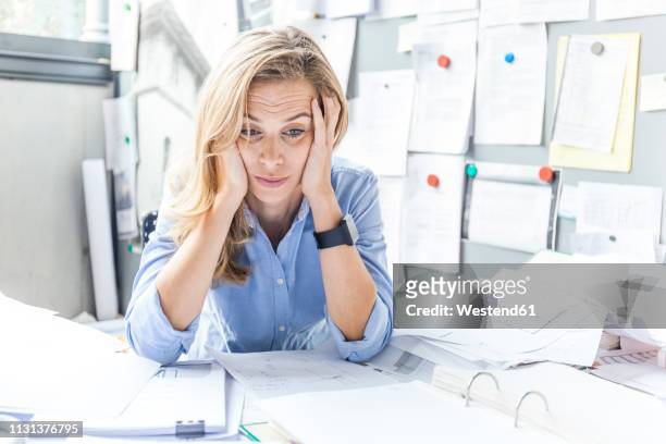 stressed woman sitting at desk in office surrounded by paperwork - frustración fotografías e imágenes de stock