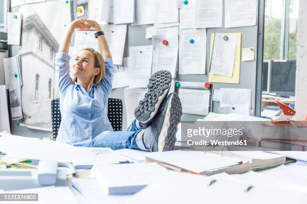 woman relaxing at desk in office surrounded by paperwork - couch potato stock-fotos und bilder