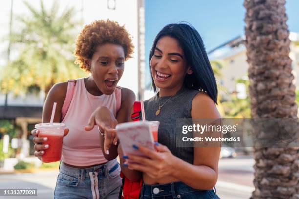 usa, florida, miami beach, two happy female friends with cell phone and soft drink in the city - tourist talking on the phone stock pictures, royalty-free photos & images