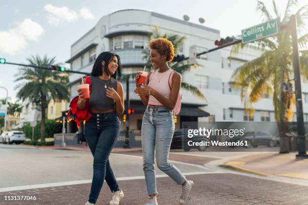 usa, florida, miami beach, two happy female friends having a soft drink crossing the street - miami people stock pictures, royalty-free photos & images