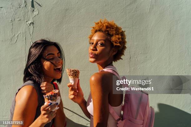 two happy female friends with ice cream cones posing at a wall - freundinnen urlaub sommer eis stock-fotos und bilder