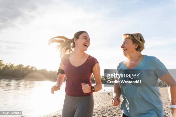 granddaughter and grandmother having fun, jogging together at the river - two woman running fotografías e imágenes de stock