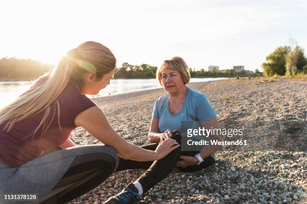 granddaughter examining aching knee of her grandmother after training at the river - female knee pain stock-fotos und bilder