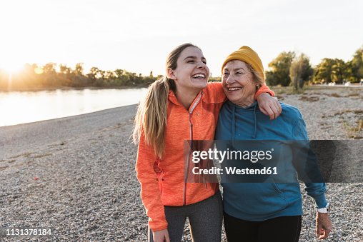 Fit grandmother and granddaughter walking at the river with arms around, having fun Fit grandmother and granddaughter walking at the river with arms around, having fun