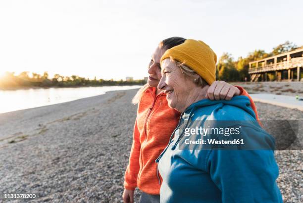 fit grandmother and granddaughter walking at the river with arms around, having fun - multi generation family thinking stock pictures, royalty-free photos & images