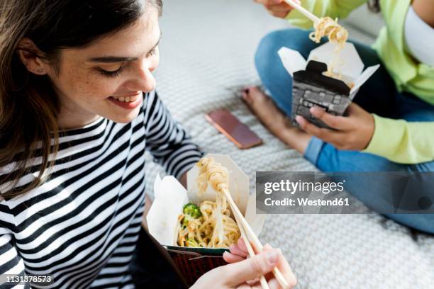 two happy young women having asian takeaway food at home - chinese takeout stock pictures, royalty-free photos & images