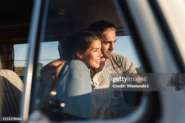 affectionate couple sitting in their camper with arms around, watching sunset - embracing car stock pictures, royalty-free photos & images