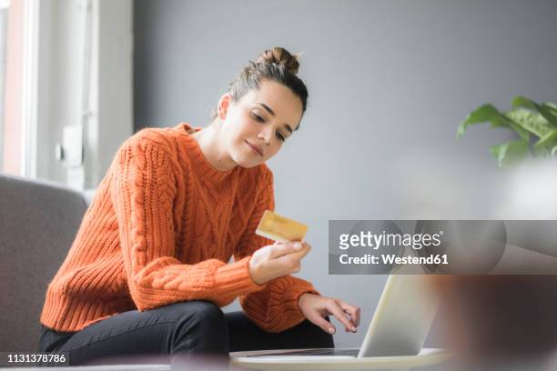 portrait of content woman sitting on couch using laptop and credit card - credit card stock-fotos und bilder
