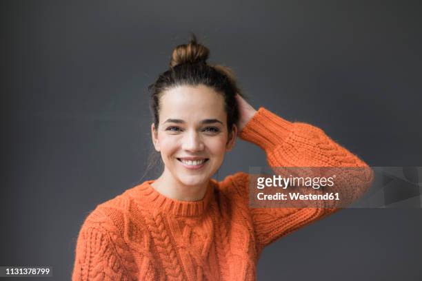 portrait of happy woman wearing orange knit pullover against grey background - haarknoten stock-fotos und bilder