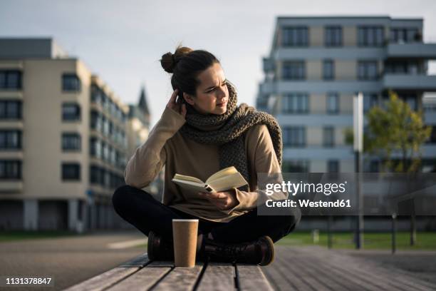 melancholy woman with coffee to go and book sitting on bench in autumn - twilight book stock pictures, royalty-free photos & images