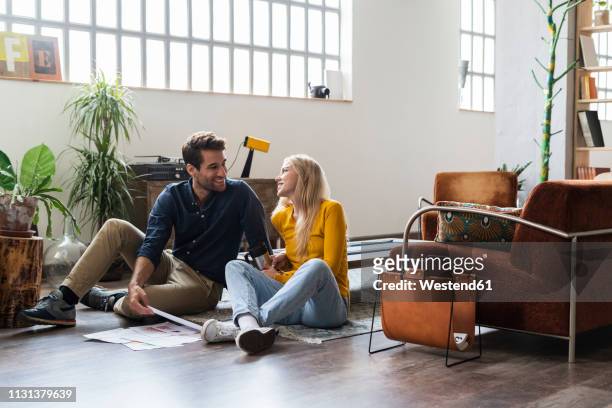 smiling businessman and businesswoman sitting on the floor discussing documents in loft office - sitting on floor fotografías e imágenes de stock