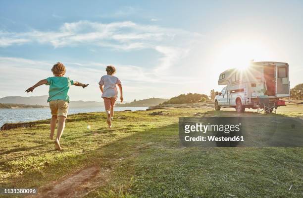 chile, talca, rio maule, two boys running on meadow beside camper at lake - camping kids photos et images de collection
