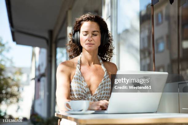 mature woman sitzting in cafe, wearing headphones, using laptop - essen germany bildbanksfoton och bilder