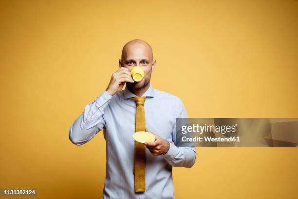 portrait of bald businessman drinking cup of coffee against yellow background - yellow shirt stock pictures, royalty-free photos & images